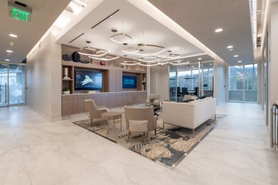 Modern office lounge in Birmingham, Alabama, featuring contemporary seating, a patterned rug, wall-mounted TV with Cisco technologies, display shelves, and a glass-walled meeting room in the background.