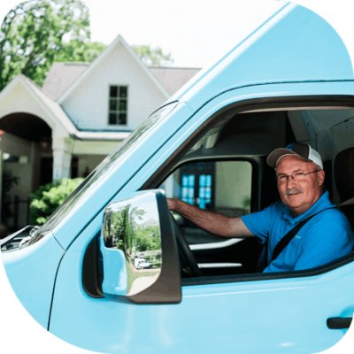 Two people wearing gray pants and bright blue athletic shoes are standing on pavement near a vehicle tire.