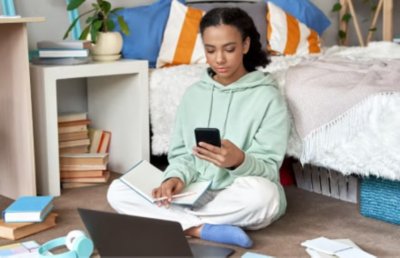 Girl sitting by bed on phone with laptop