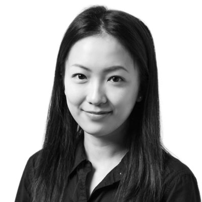 A woman with long, straight hair wearing a dark button-up shirt, facing forward and smiling slightly against a plain background.