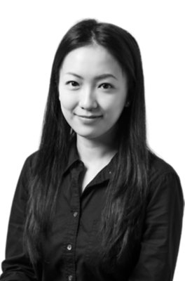 A woman with long, straight hair wearing a dark button-up shirt, facing forward and smiling slightly against a plain background.