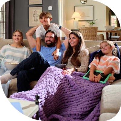 A smiling family of five sits together on a couch in a cozy living room.
