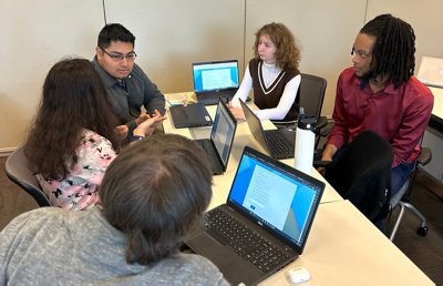 Group of interns having a discussion while working on laptops