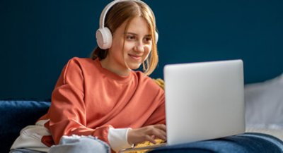 Teenage girl on bed with headphones and laptop