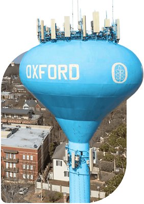 A tall blue water tower labeled "OXFORD" with antenna equipment on top, standing above nearby residential buildings.