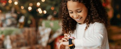 GIrl playing on Xplora smart watch with Christmas tree in the back